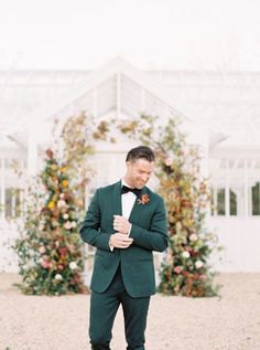 a man in a green suit and bow tie standing next to a white building with flowers