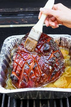 someone using a spatula to brush the top of a roasting pan filled with ribs