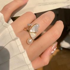 ✦ Embrace the romantic feel of a fairy garden with this elegant and sacred pearl and ivory ring, adorned with tiny inlaid zircon. A perfect hue of gold adds a touch of sophistication, making it the perfect accessory for any occasion. From bridesmaids to sisters, this cocktail split ring is a heartfelt gift that will be cherished for years to come. Add a touch of magic to your dinner parties or nights out with this exquisite piece. ----------- DETAILS ----------- - Color: Gold, Ivory - Ring Size: Adjustable - Materials: Gold Plated, Faux Pearl, Cubic Zirconia - SKU: K4113 Exquisite Gold Pearl Ring For Wedding, White Flower Ring With Diamond Accents For Wedding, Elegant Gold Butterfly Ring With Diamond Accents, Elegant Gold Diamond Butterfly Ring, Dainty White Crystal Ring, White Elegant Rings, Pearl White Open Ring Pearl Jewelry, Gold Crystal Ring For Wedding, Elegant Butterfly Ring With Diamond Accents For Wedding