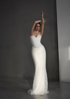 a woman in a white wedding dress posing for the camera with her arms up and hands behind her head