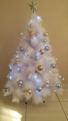 a white christmas tree decorated with gold and silver ornaments is on the floor in front of a beige wall