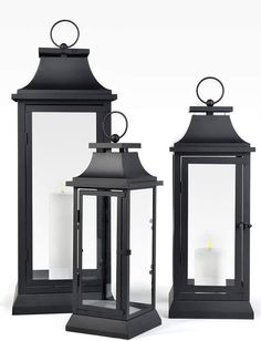 three black lanterns sitting side by side next to each other with one candle lit in the middle