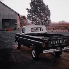 an old black and white chevrolet truck parked in front of a barn with a tree