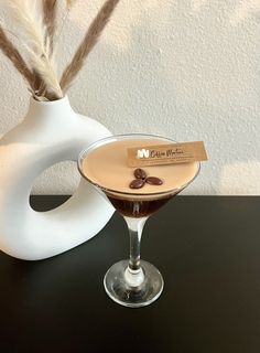 a martini glass sitting on top of a table next to a white vase with feathers sticking out of it