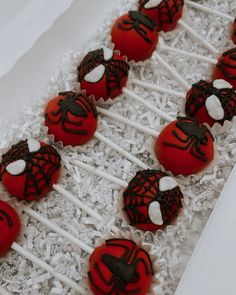 red and black cake pops with spiderman faces on them sitting in a white box