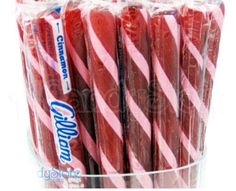 candy canes wrapped in pink and white striped plastic wrappers are stacked up in a clear container