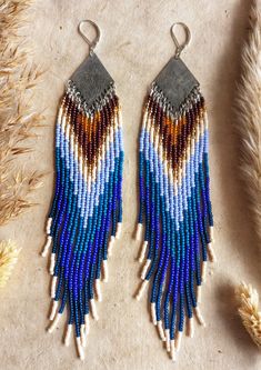 two pairs of beaded earrings sitting on top of a table next to dried grass