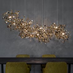 a modern chandelier hanging over a dining room table with yellow chairs and a dark gray wall