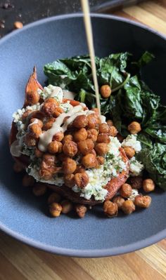 a blue plate topped with spinach and chickpeas covered in ranch dressing on top of a wooden table