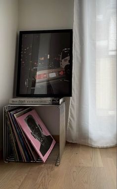 a stack of records sitting on top of a metal shelf next to a window with white curtains