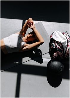 a woman laying on the ground next to a ball and backpack with her hands behind her head