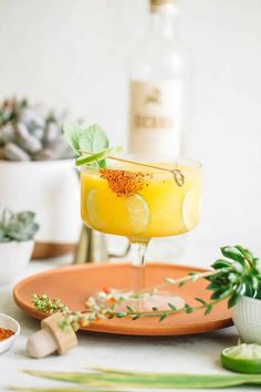 a glass filled with yellow liquid sitting on top of a plate next to some succulents