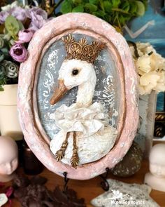 a white duck with a crown on its head in a pink frame next to flowers