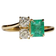 an emerald and diamond three stone ring with two gold bands on each side, set against a white background