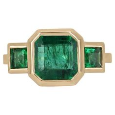 Introducing our exquisite Emerald Trilogy Ring, featuring a magnificent 3.08-carat Asscher-cut emerald as the focal point, radiating with a rich dark green hue and transparent clarity. Complemented by a princess-cut emerald on each side, set in lustrous 14k yellow gold bezels, this ring exudes elegance and sophistication. Elevate any ensemble with this timeless piece that captures the allure of nature's finest treasures. Setting Style: Bezel-Three Stone Setting Material: 14K Yellow Gold Setting Luxury Women's Asscher Cut Emerald Ring, Luxury Formal Asscher Cut Emerald Ring, Luxury Asscher Cut Green Diamond Ring, Luxury Asscher Cut Green Ring, Luxury Green Asscher-cut Rings, Emerald Three Stone Ring, Ring Princess Cut, Trilogy Ring, Emerald Diamond Ring