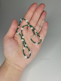 a person's hand holding some green and white beads