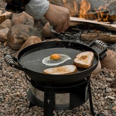 someone is frying eggs in a skillet on an open fire pit with rocks