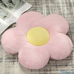 a pink flower shaped pillow sitting on top of a bed next to a magazine and magazines