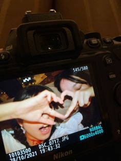 a person making a heart shape with their hand on a camera lens that is attached to the back of a digital camera