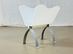 a white chair sitting on top of a metal stand in front of a white wall