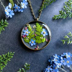 a necklace with blue flowers and green leaves in it on a black surface next to some branches