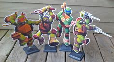 three paper cutouts of teenage mutant ninjas on wooden deck with fence in background