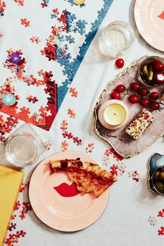 a table topped with plates and bowls filled with pizza next to candles, glasses and fruit