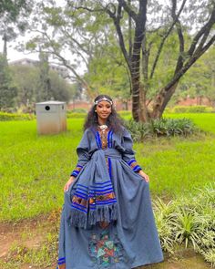 a woman standing in front of a tree wearing a blue dress and headpieces