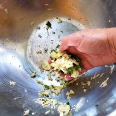 a hand picking up food from a metal bowl