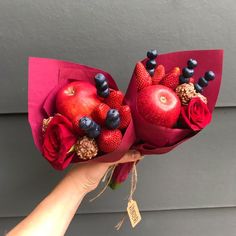 someone is holding some flowers and fruit in front of a wall with a sign on it