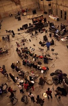 a group of people are sitting in a large room with instruments and music equipment on the floor