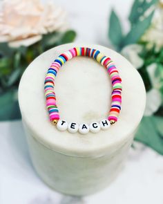 a colorful beaded bracelet with the word teach on it sitting next to some flowers