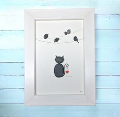 a black cat sitting on top of a white frame next to two birds hanging from a wire