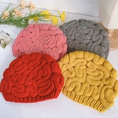 four knitted beanies sitting next to each other on top of a white table