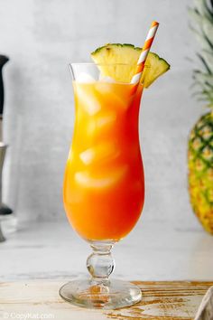 an orange drink in a glass with a pineapple on the side