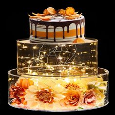 three tiered cake with flowers and lights on it's sides, in front of a black background