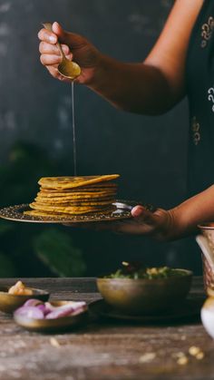 a woman is holding a plate with food on it and she is drizzling something over the top