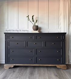 a black dresser with gold knobs and flowers in a vase on it's top