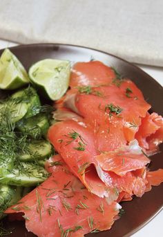 salmon and cucumbers on a plate with dill, lemon wedges and lime slices