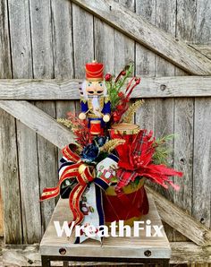 a nutcracker arrangement in a red vase on a wooden table next to a fence