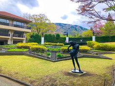 a statue is in the middle of a grassy area next to a building and trees