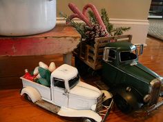 two toy trucks with christmas decorations in them on a wooden table next to a potted plant