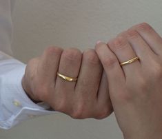 two hands holding each other with gold rings on their fingers, both wearing white shirts