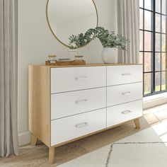 a white dresser sitting next to a window with a round mirror on top of it