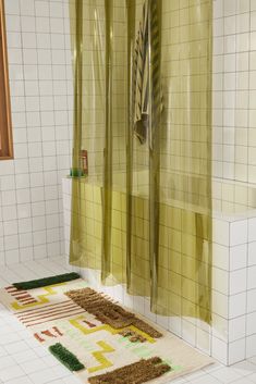 a bath room with a rug on the floor next to a shower curtain and tiled walls