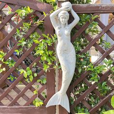 a statue of a mermaid holding a ball in her hand on the side of a fence