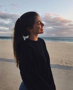 a woman is standing on the beach with her hair in a pony tail and looking off into the distance