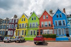 a row of multi - colored houses on the corner of a street with cars parked in front