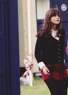 a woman standing in front of a blue door wearing a red skirt and black cardigan