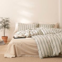 a bed with white and green striped comforter next to a small potted plant